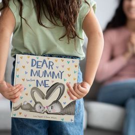 Child holding book behind back to gift to mum.